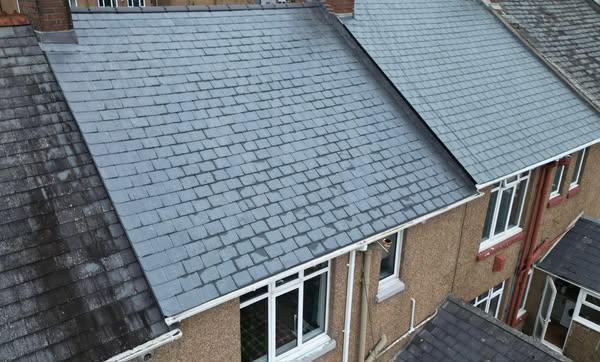 Aerial view of terraced houses with slate roofs. The central roof appears newer and cleaner compared to the adjacent older, darker roofs. The houses have light brown exteriors and white-framed windows.