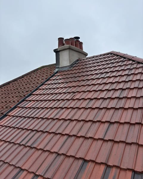 A sloped roof covered with red tiles is shown against a cloudy sky. A chimney with several pots is visible near the top of the roof.